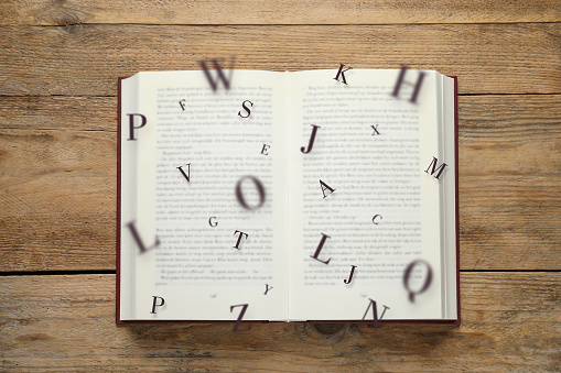 Open book with letters flying out of it on wooden background, top view