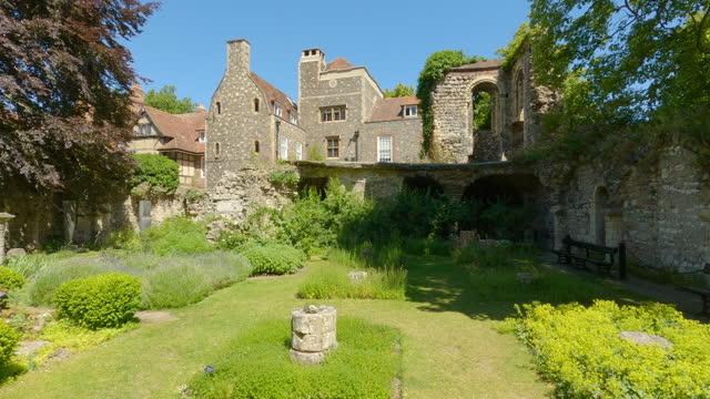Stone walls and wooden benches surrounding herb garden with a view of old houses