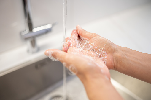 Woman washing hands with soap and water under bathroom faucet close up