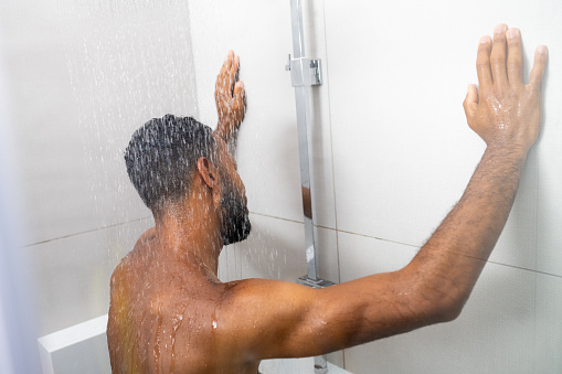 Multiracial man standing under running water in shower, back side view