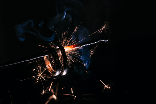Wedding rings on burning bengal light with many sparks on dark background. Marriage proposal for Christmas.