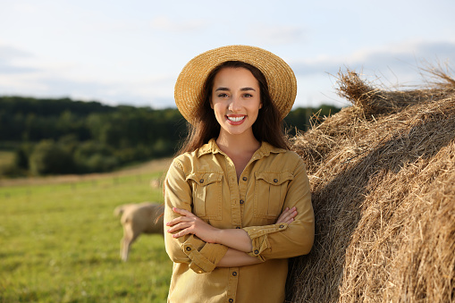 Smiling woman near hay bale on animal farm. Space for text