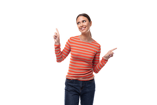 a slender young brunette woman dressed in a tight-fitting orange sweater points her fingers at an empty space.