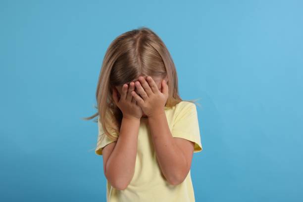 istock Resentful girl covering face with hands on light blue background 1885895404