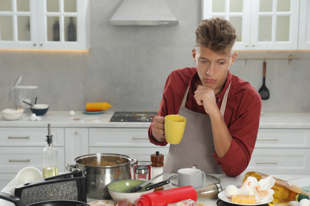 istock Upset man drinking tea in messy kitchen. Many dirty dishware, utensils and food leftovers on table 1885899898