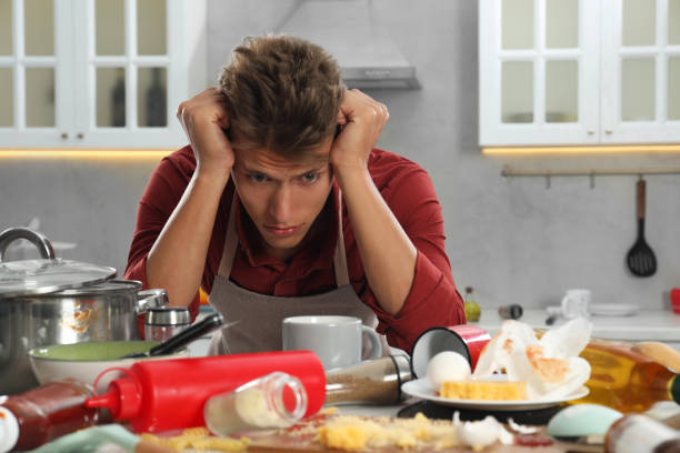 istock Upset man in messy kitchen. Many dirty dishware, utensils and food leftovers on table 1885901101
