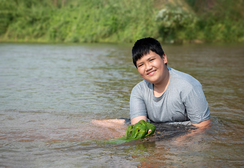 Asian boy holds freshwater algae that he plucks from a river to study the river's cleanliness, idea for ecosystem, ecoeffect and pesticide effect.