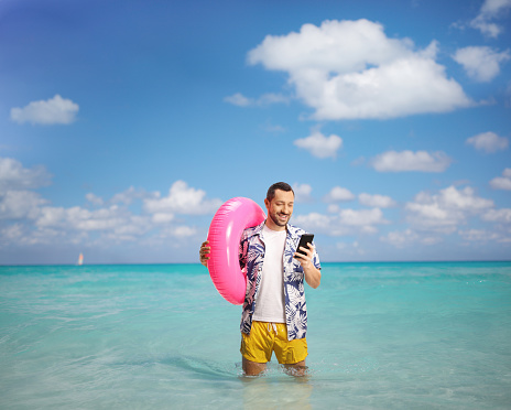 Happy young man browsing on a smartphone and holding a swimming ring in the sea