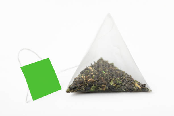 Tea Time. Pyramidal green tea bag with a green label on a white background. Tea bag pyramid shape. Close-up