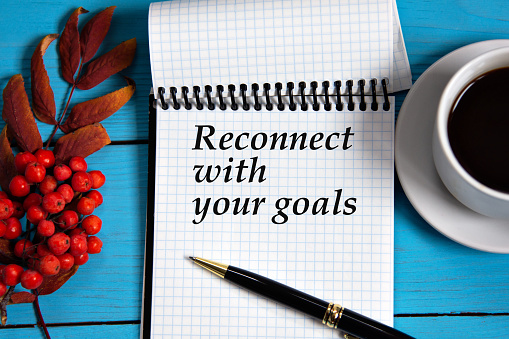 RECONNECT WITH YOUR GOALS - words in a white notebook on a wooden blue background with a rowan branch and a fragment of a cup of coffee. Info concept