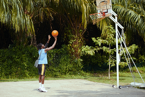 Black man throwing ball in basket when playing alone on basketball court