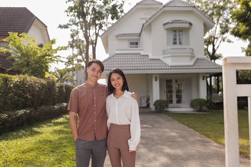 Portrait of smiling couple looking at camera in front of their newly purchased home.