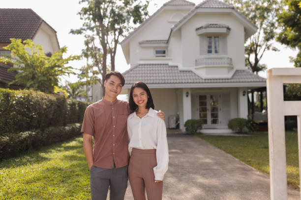 Smiling couple in front of their new house Portrait of smiling couple looking at camera in front of their newly purchased home. asian young couple stock pictures, royalty-free photos & images