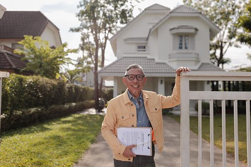 Portrait of a senior real estate agent looking at camera and smiling in front of the house for sale.