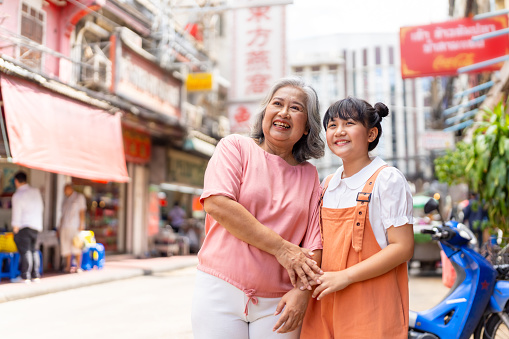 Happy Asian family grandmother and grandchild girl walking and shopping together at street market. Senior woman and little girl enjoy and fun outdoor lifestyle travel in the city on summer vacation.