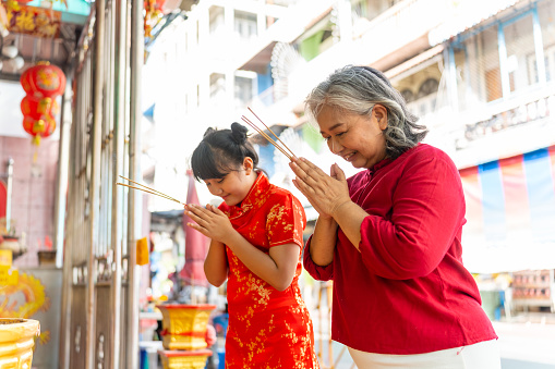 Chinese lunar new year festival and tradition holiday celebration concept. Happy Asian family grandmother and grandchild girl praying a wish with incense and red candle together at Chinese shrine.