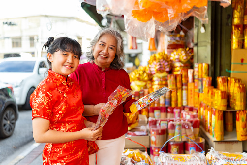 Portrait of Happy Asian family grandmother and grandchild girl choosing and buying home decorative ornaments for celebrating Chinese Lunar New Year festival and traditional holiday together at Chinatown street market.