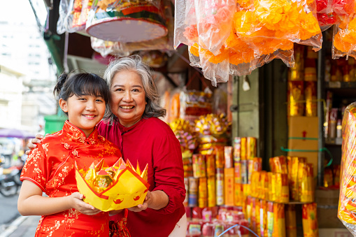 Happy Asian family grandmother and grandchild girl choosing and buying home decorative ornaments for celebrating Chinese Lunar New Year festival and traditional holiday together at Chinatown street market.