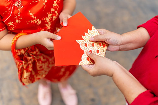 Chinese lunar new year festival and tradition holiday celebration concept. Happy Asian family grandmother giving red envelope contained money gift with blessing to little grandchild girl in Chinese red dress.