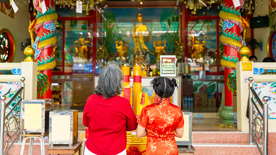 Chinese lunar new year festival and tradition holiday celebration concept. Happy Asian family grandmother and grandchild girl praying a wish with incense and red candle together at Chinese shrine.