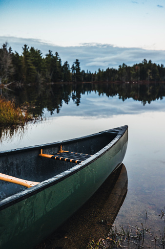 Green canoe sits on the edge of tranquil pond in the Maine woods in Millinocket, Maine, United States