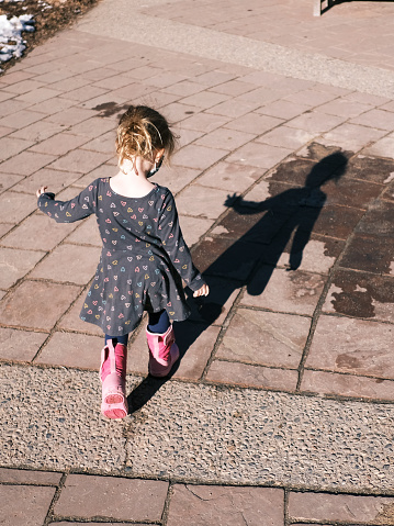 Child in casual clothing walking along footpath in spring sunlig in Denver, Colorado, United States