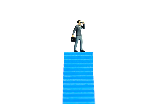 Miniature tiny people toys photography. Businessman using binocular telescope standing above blue stairway. Isolated on a white background. Image photo