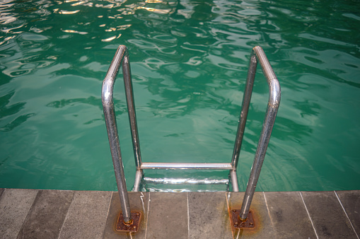 a stainless steel swimming ladder in a swimming pool with turquoise water