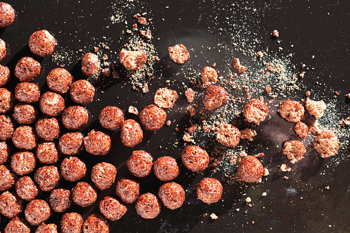 Chocolate cornflakes balls, whole and broken, on a black tray close-up, top view
