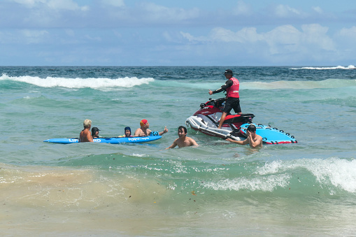Two adults and two children got into difficulty in the most dangerous part of Bondi Beach and were rescued by a lifeguard on a jet ski, lifeguard with a surfboard and a volunteer surf lifesaver. The surf lifesaver, wearing the traditional red and yellow hat, gives the 