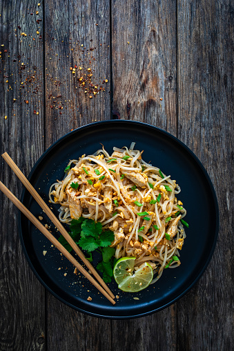 Pad Thai with chicken nuggets and rice noodles in peanut and tamarind sauce on wooden table