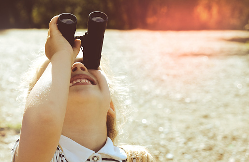 Little girl using binoculars in the forest. Exploring the world. Outdoor activities.