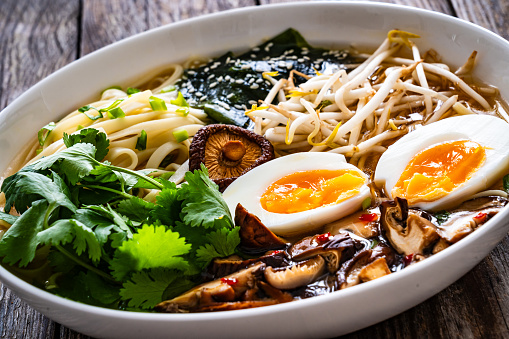 Asian style soup. Broth with chow mein noodles, boiled eggs, shiitake mushrooms, cilantro and mung sprouts on wooden background