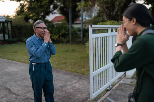 A senior host warmly welcomes a man to his vacation rental and greets him in front of the house.