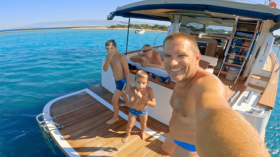 Smiling family taking selfies on yacht while enjoying in sea during sunny day.