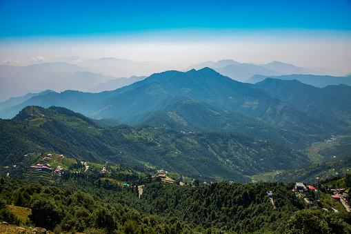 Mussourie hill station view with green lush mountain and blue cloudy sky in the Indian state of Uttarakhand.