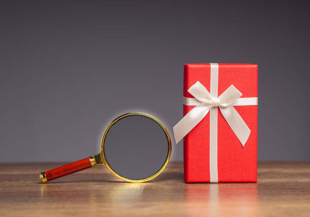Red gift box and a magnifying glass on a wooden table.