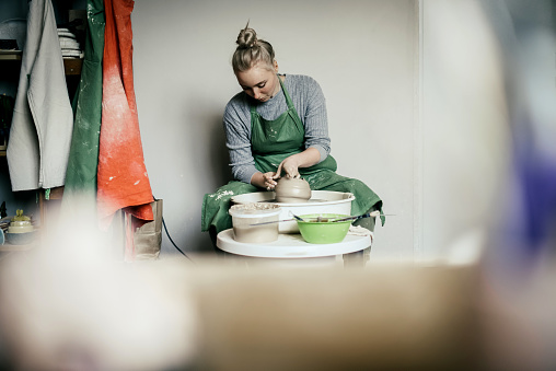 Woman potter moulding walls of clay ware on potters wheel