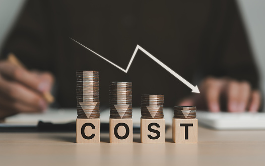 Cost reduction concept. Cost wording on decreasing coins stacking with the down arrow. Businessman working on company cost saving. Cost Management, Economy recession, low budget, Effective business,