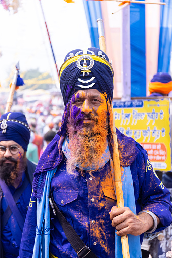 Anandpur Sahib, Punjab, India - March 2022: Portrait of sikh male (Nihang Sardar) during the celebration of Hola Mohalla at Anandpur Sahib during holi festival. Selective focus on colorful face.