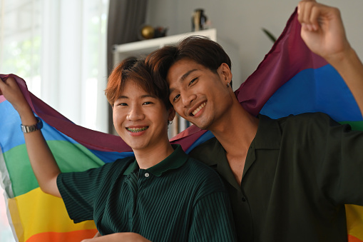 Close up with Asian teenage gay couples looking at camera and holding rainbow flags together, Support and celebrate the LGBT community.