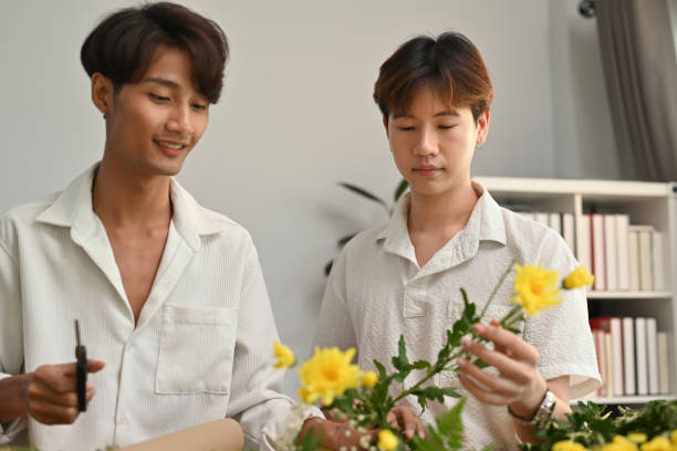 portrait with asian gay couple, they are helping to arrange a bouquet of flowers in the house. - florist flower arranging male стоковые фото и изображения