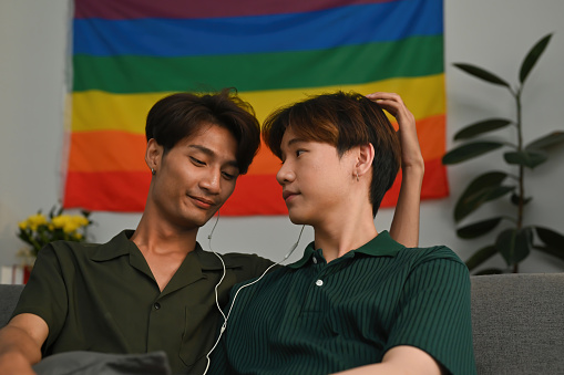 Young gay millennials look sweetly at their boyfriends while listening to music together.
