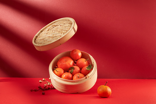 Tangerines are stored in a bamboo steamer on a red background. Tangerines are meant to bring good luck at the beginning of the year. Tet theme.