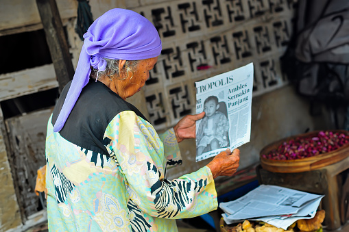 Pasuruan, Indonesia - April 11th, 2012 : an old woman was reading the torn newspaper that was used to wrap her merchandise