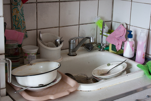 Dirty dishes in sink waiting to be washed. Dirty sink in apartment kitchen. Unsanitary conditions. Old dishes. Dirt everywhere.