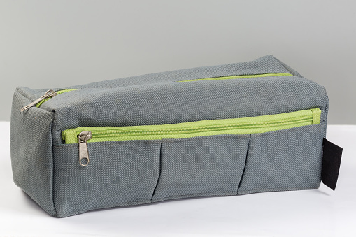 Small fabric gray travel toiletry bag with two green zippered closures lies on a white surface on a gray background