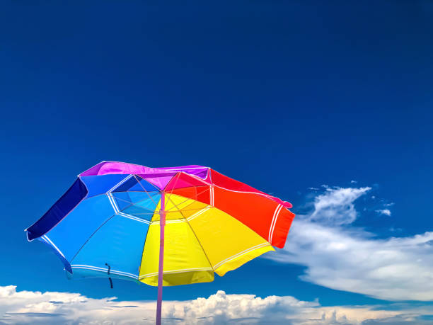 A rainbow of colors are represented in this brightly colored beach umbrella. It is shot from below and there is a blue sky with low cumulus clouds at the bottom.  There is amble copy space. Image is taken from Panama  City Florida on Gulf Coast.