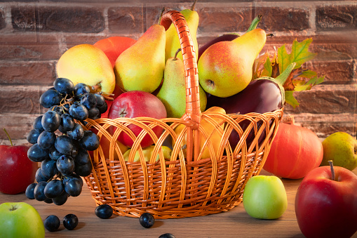 Ripe apples, pears, grapes, pumpkin, eggplants in a wicker basket near a brick wall