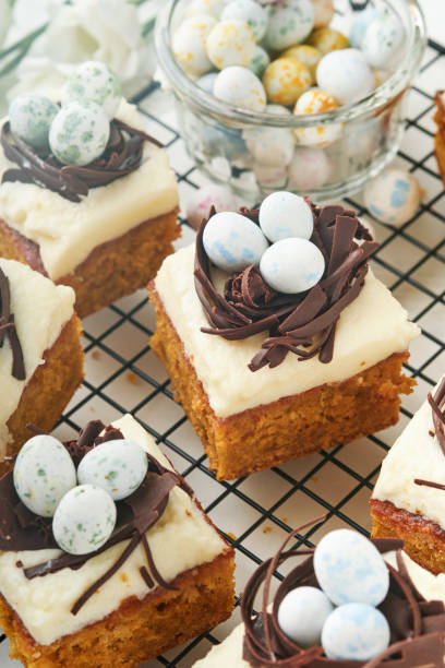 istock Easter carrot cake bars decorated with chocolate nest and chocolate candy eggs blossoming cherry or apple flowers on rustic light wooden backgrounds. Easter holiday meal. Traditional Easter food. 1886770477